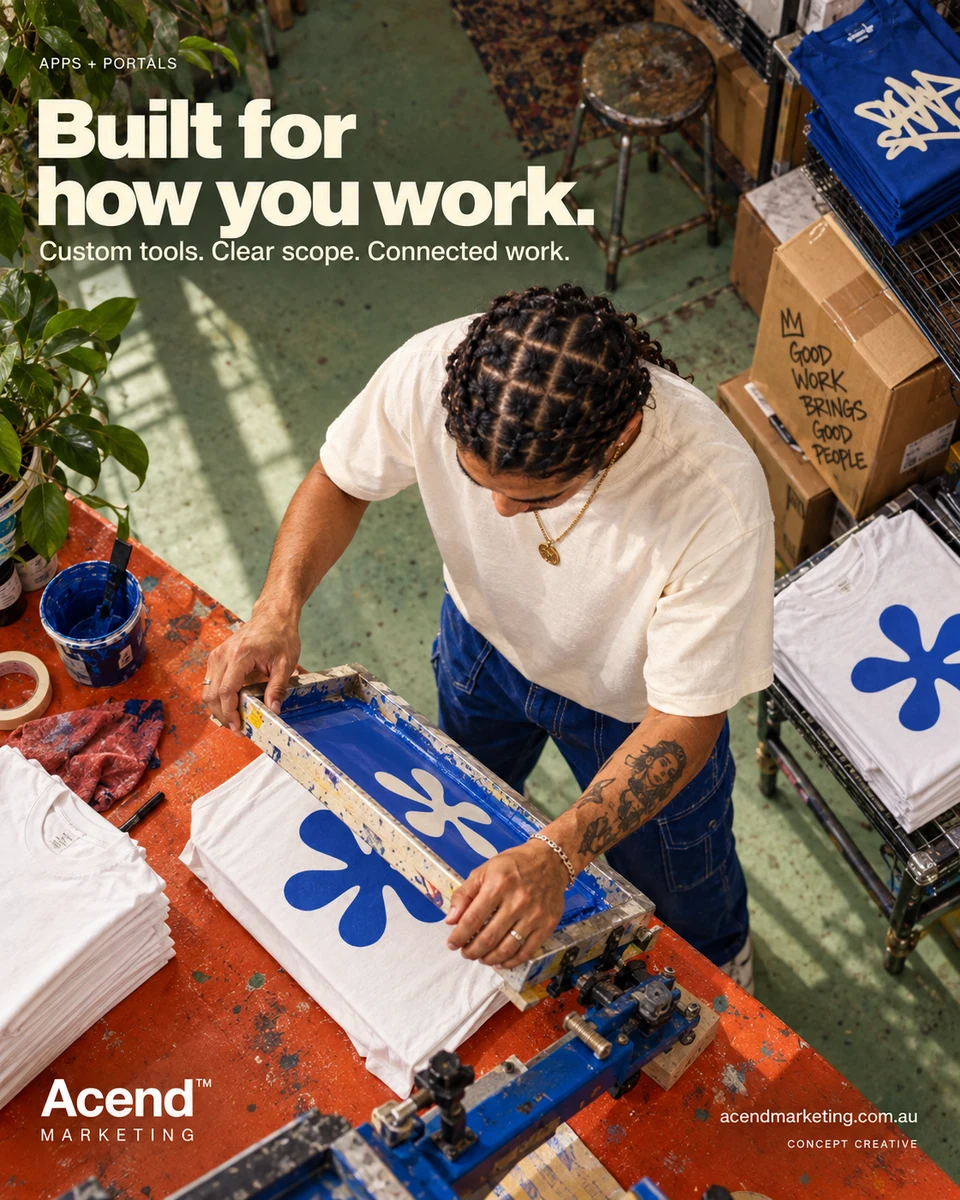 Overhead concept photograph of a person lifting a printing screen above a white shirt with a cobalt design on an orange workbench. Blank shirts, finished garments and boxes surround the station. Acend Apps + Portals: “Built for how you work.” Custom tools, clear scope, connected work.